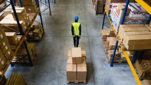 Man pulling a cart with a box inside a warehouse, illustrating workplace lifting and material handling tasks.